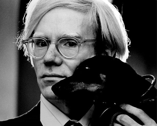 Andy Warhol holds a pet dachshund dog to his cheek